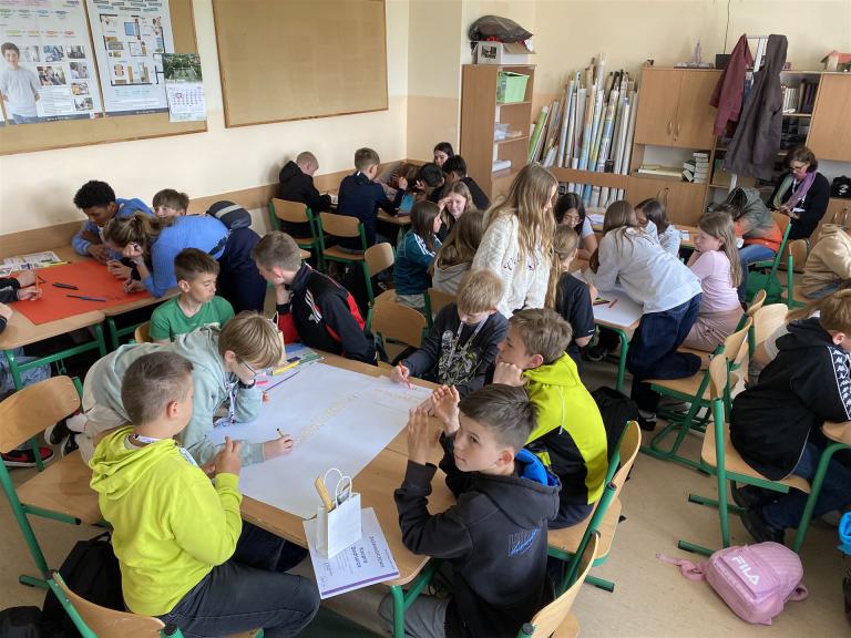 Das Foto zeigt einen Klassenraum mit vielen Schülerinnen und Schülern an Gruppentischen arbeiten